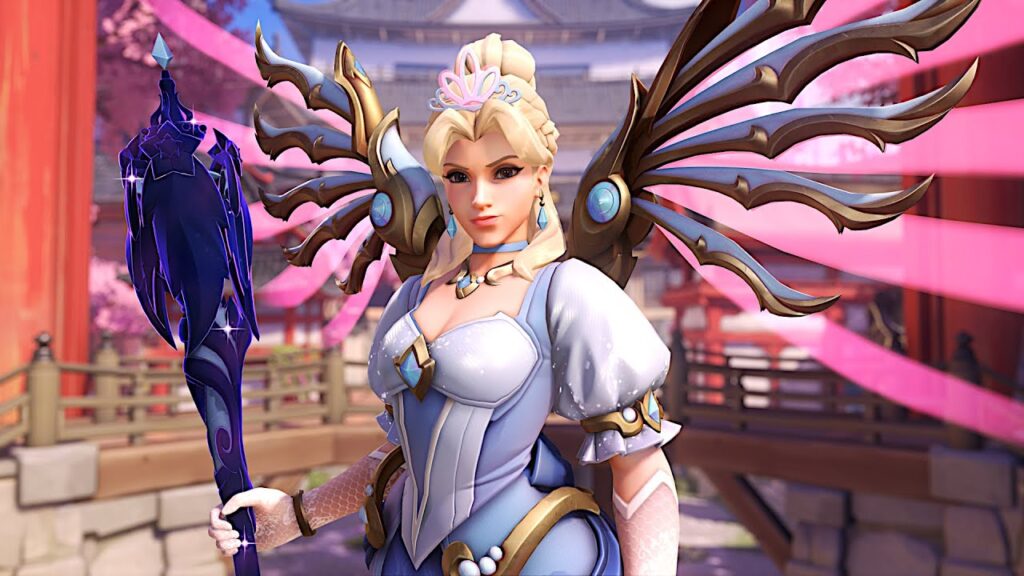 Royal Princess Mercy in a blue and white winged costume with golden accents holds a dark ornate staff