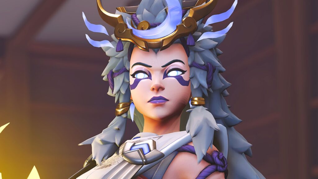 Close-up of Kiriko in her mythic skin from Overwatch 2, featuring glowing white eyes, elaborate silver and purple armor, and a moon-shaped crown with mystical elements.