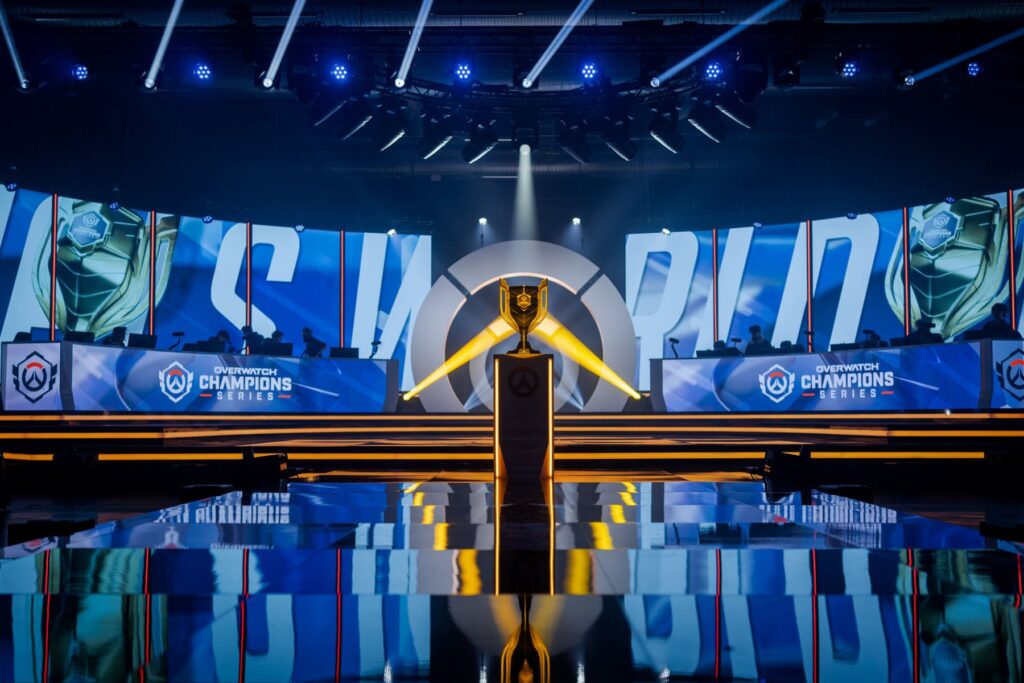 An esports arena set for the Overwatch Champions Series, featuring a trophy at center stage and illuminated screens in the background.